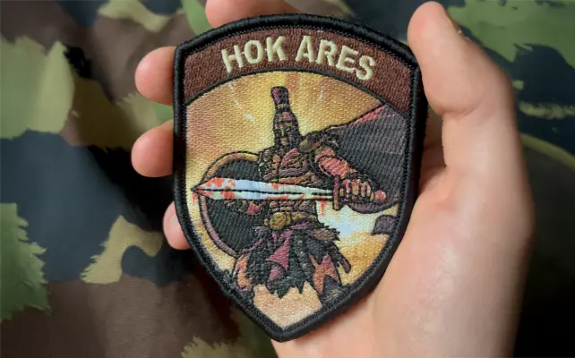 Zugbadge ricamato "HOK ARES" con figura guerriera e spada, motivo militare scuro in stile svizzero.